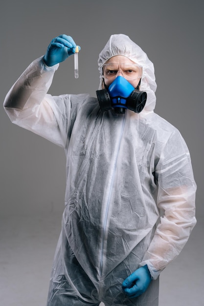 Scientist in protective suit, goggles and respirator is holding test tube in hand. concept of working on coronavirus vaccine. studio shot on dark background