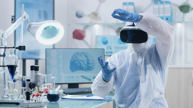 Scientist researcher doctor wearing virtual reality headset analyzing brain activity during neuroscience experiment in biochemistry hospital laboratory. Specialist neurologist checking infographics