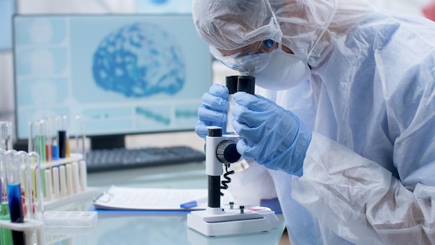 Scientist researcher in ppe equipment looking into microscope\
analyzing dna sample working at coronavirus vaccine development\
during microbiology experiment in hospital laboratory. medicine\
concept