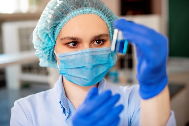 Scientist researching in laboratory and holding blue solution into the glass cuvette