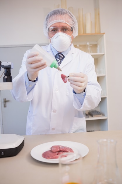 Scientist sprinkling fluid on meat 