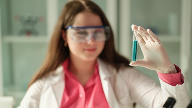 Ученая студентка смотрит на синий раствор и пробирку, работающую в оборудованной лаборатории
