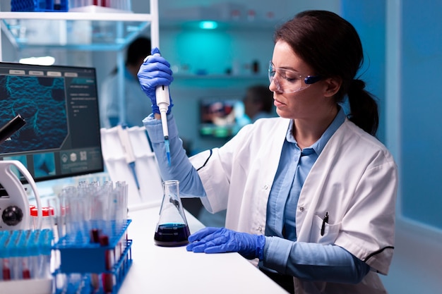 Scientist taking sample with micropipette wearing glasses in modern laboratory