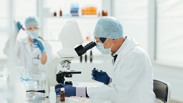 Ученый с помощью микроскопа в биохимической лаборатории