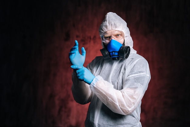 Scientist wearing hazmat goggles and respirator slips on hands rubber gloves