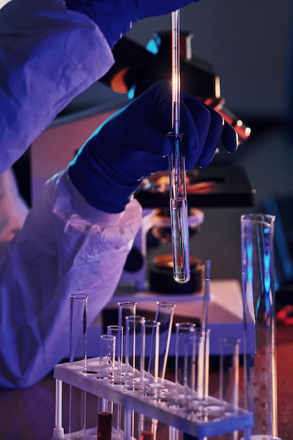 Lo scienziato in uniforme protettiva bianca lavora con coronavirus e provette di sangue in laboratorio