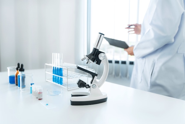 Scientist woman standing to reading result coronavirus vaccine on report after using microscope and test tube with blue liquid to experiment produce vaccine covid-19 in laboratory