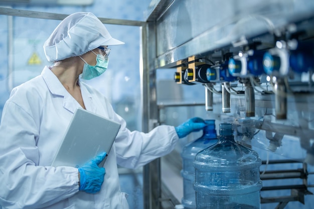 Foto lavoratore scientifico che controlla la qualità delle bottiglie d'acqua sulla linea di trasporto delle macchine in fabbrica