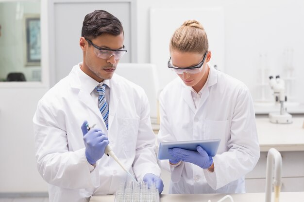 Scientists examining tubes in tray using tablet pc 