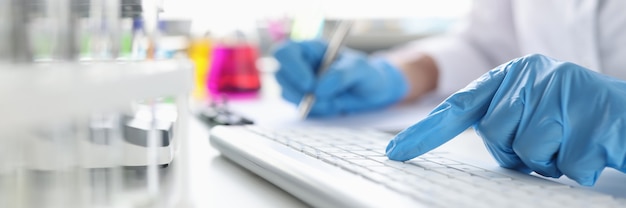 Foto scienziati con le mani nei guanti che lavorano sulla tastiera durante il lavoro scientifico desktop sulla medicina