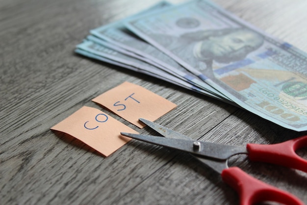 Scissor money and note with text COST Financial cost cutting reduce expenses concept