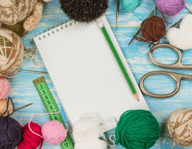 Scissors, balls of wool, measuring tape and notebook on a wooden table.