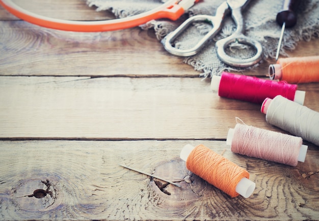 Scissors, bobbins with thread and needles, striped fabric. Old sewing tools on the old wooden