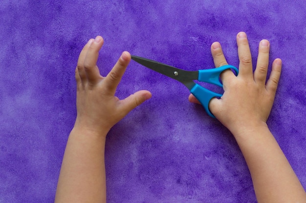 Photo scissors in child hands on the purple background