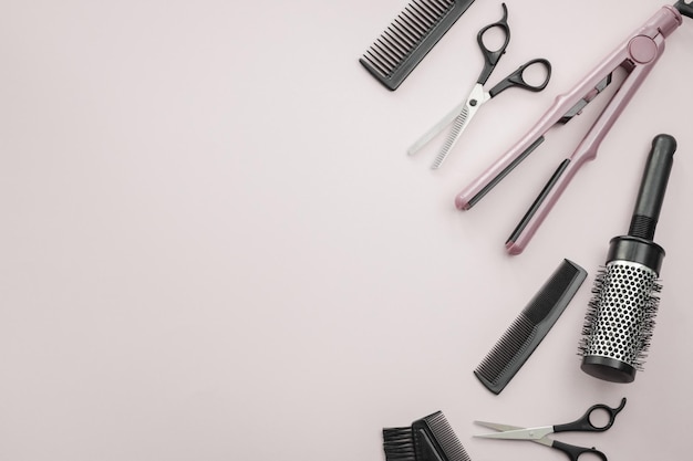 Scissors combs brushes and a hair straightener on a pale pink background