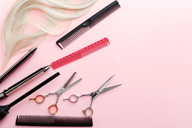 Photo scissors, combs, hair iron and other hairdresser's accessories and strand of blonde hair on pink background. hairdresser service.