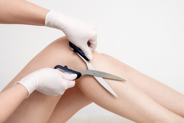 Forbici nelle mani della donna che taglia i capelli sulle gambe. concetto di depilazione.