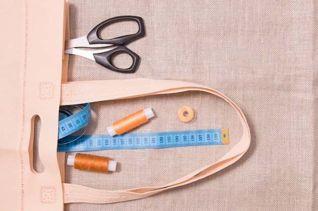 Фото Ножницы, рулетка и несколько мотков ниток в эко-сумке на льняной ткани.