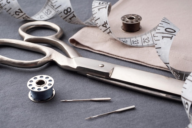 Scissors spools of thread needles and a centimeter lie on the dark gray fabric of the Tshirt Sewing accessories on the background of sewn clothes Cutting and sewing concept Tailor's Desk