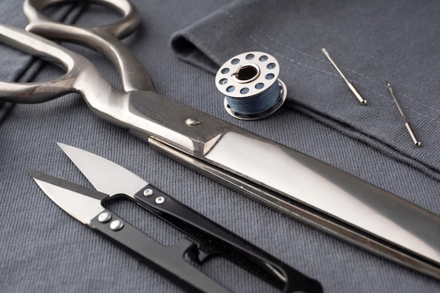 Scissors spools of thread needles and a centimeter lie on the dark gray fabric of the Tshirt Sewing accessories on the background of sewn clothes Cutting and sewing concept Tailor's Desk