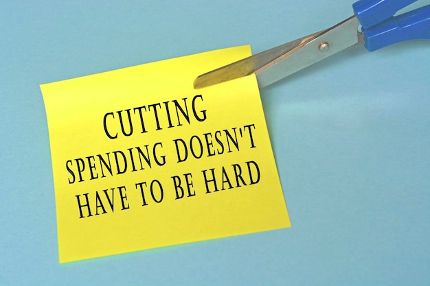 Scissors that cut yellow notepad with text on a blue background. Spending concept