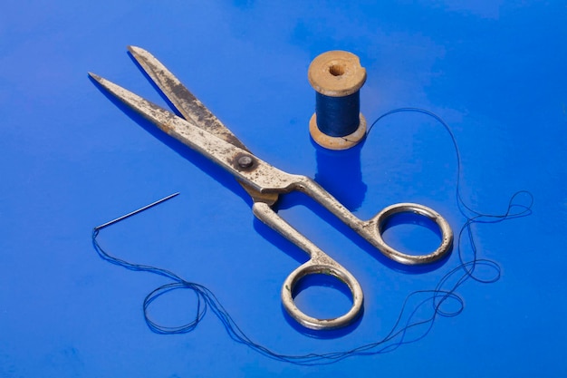 Photo scissors and thread bobbin on blue background