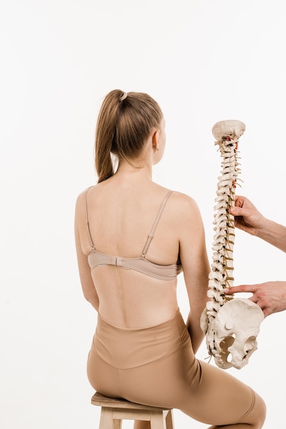 Scoliosis is sideways curvature of the spine Backbone anatomical model with young woman Orthopedist showing spinal column model with girl on white background