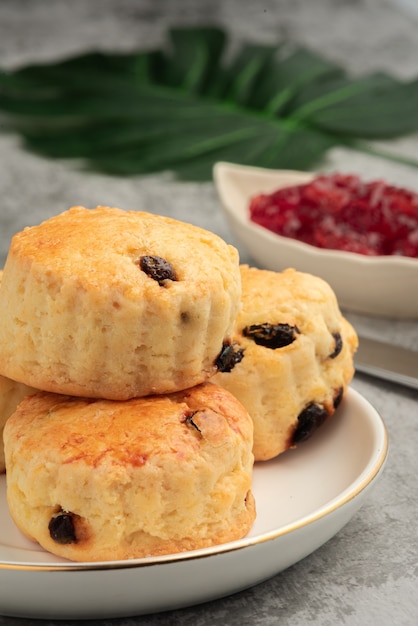 Scone in piatto bianco e marmellata di fragole su fondo di cemento