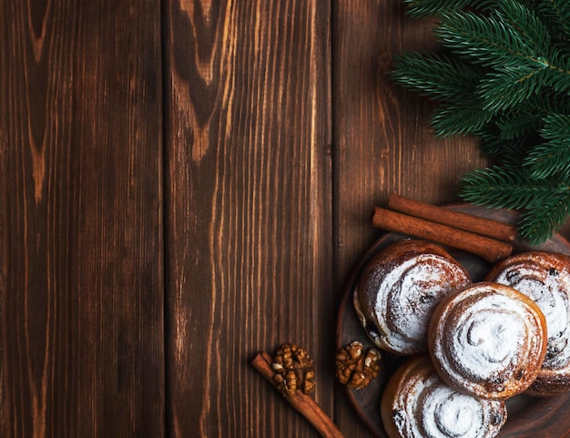 Scones on a plate with cinnamon and walnuts on a wooden background with spruce branches Top view