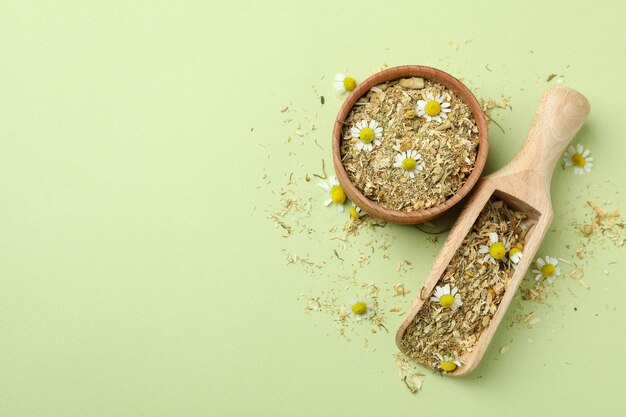 Scoop and bowl with dried chamomile on green