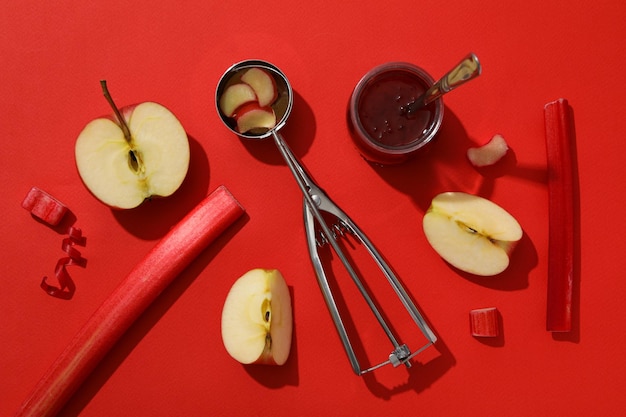 Scoop rhubarb stem jar of jam and apple on red background flatlay