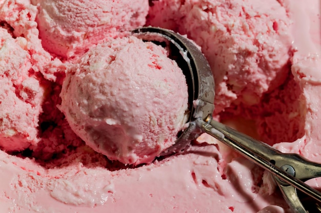Foto una pallina di gelato alla fragola con un cucchiaio rosa.