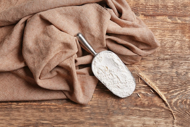 Scoop with flour and napkin on wooden table