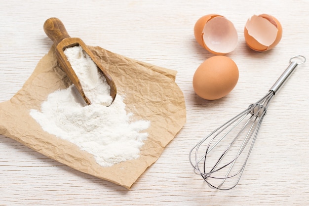 Photo scoop with flour on paper. chicken egg shell and whisk. white background. top view