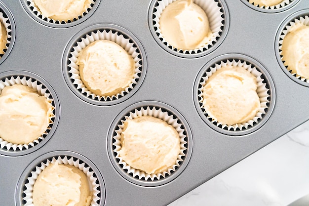 Scooping cupcake batter into cupcake pan lined with cupcake liners to bake vanilla cupcakes.