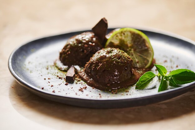 Scoops of chocolate sorbet with sprinkled matcha powder slice of lime lemon basil on dark blue plate Selective focus