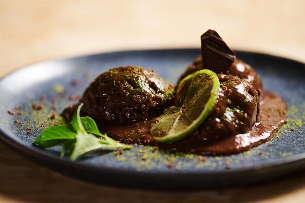 Foto palline di sorbetto al cioccolato con polvere di matcha spruzzata fetta di lime limone basilico su piatto blu scuro messa a fuoco selettiva