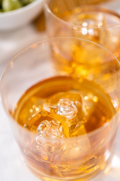 Scotch on the rocks in whiskey glass on a white marble surface.