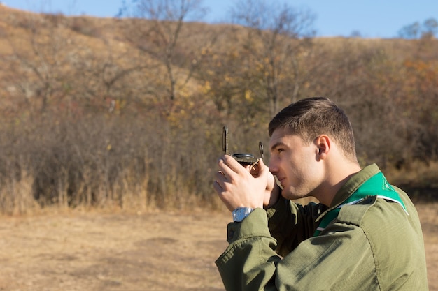 Scout or ranger taking a sighting with a compass lining it up with his eye as he traverses the wilderness using it for navigation