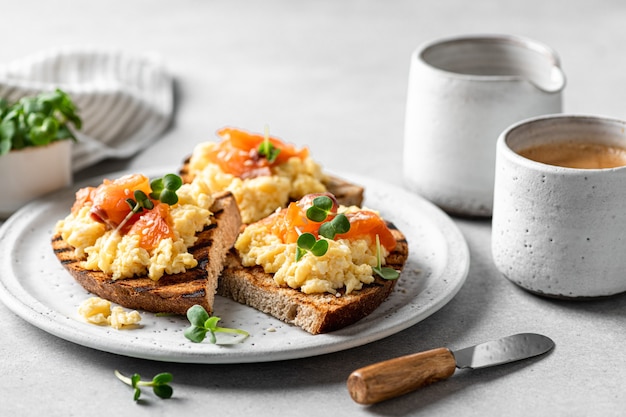 Scrambled egg sandwich with salmon on a ceramic plate on a white table, selective focus