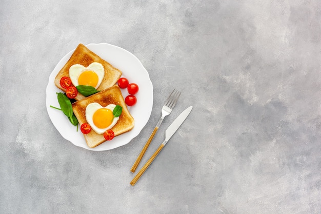 Uova strapazzate a forma di cuore sulla piastra con pomodori, verdure e caffè