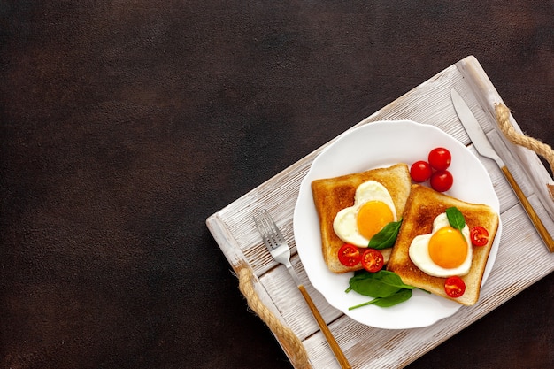 Scrambled eggs in the form of heart on plate with tomatoes, greens and coffee