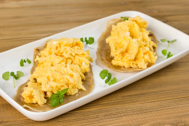 Scrambled eggs and greens in white plate.