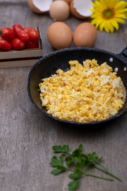 Scrambled eggs in an iron pan on the rustic wooden table