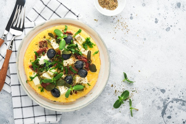 Scrambled eggs light fluffy and buttery scrambled eggs with\
feta cheese sundried tomatoes and black olives on plate over white\
stone background delicious breakfast top view flat lay