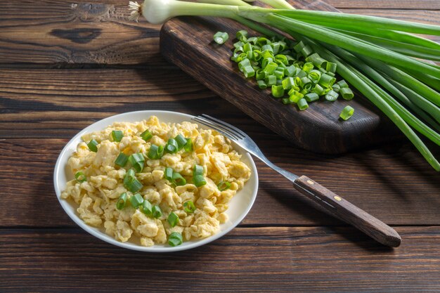 Scrambled eggs on a white plate with green onions.