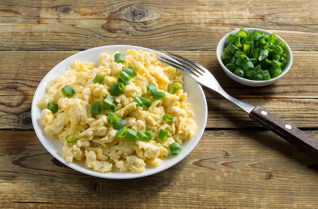 Scrambled eggs on a white plate with green onions.