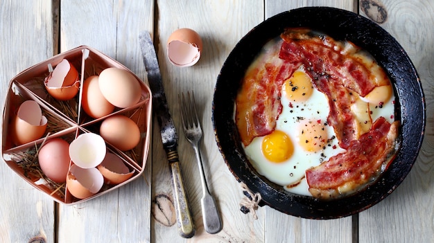 Scrambled eggs with bacon in a skillet on the table.