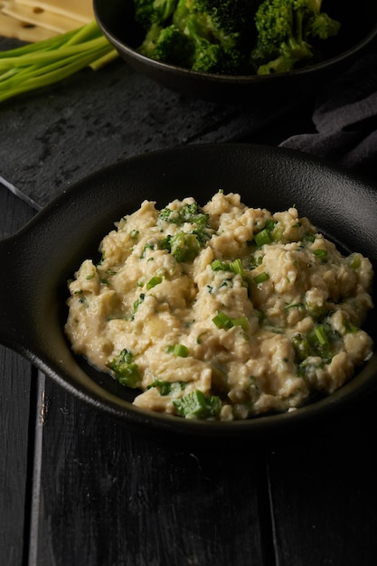 Scrambled eggs with broccoli and green onion served in dark plate with bread on table