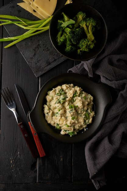 Scrambled eggs with broccoli and green onion served in dark plate with bread on table